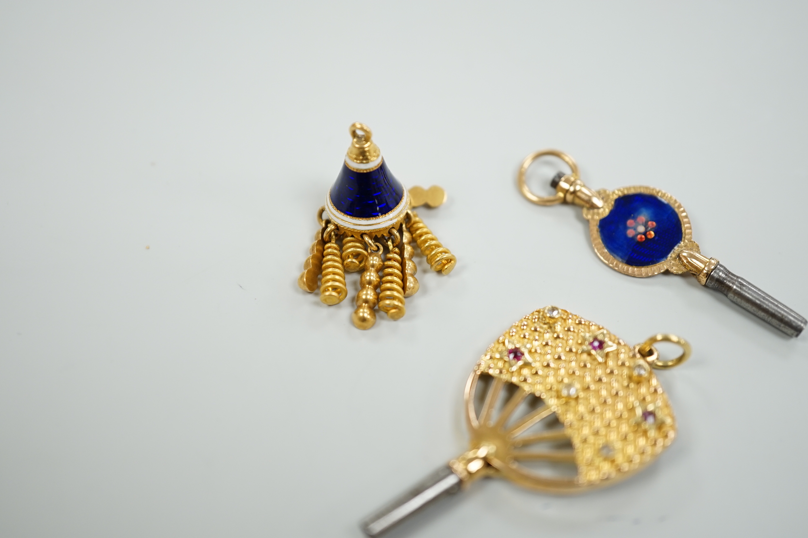 An early 20th century yellow metal (stamped 15), ruby and diamond set watch key, 39mm, together with a three colour enamelled watch key and an enamelled tassel charm.